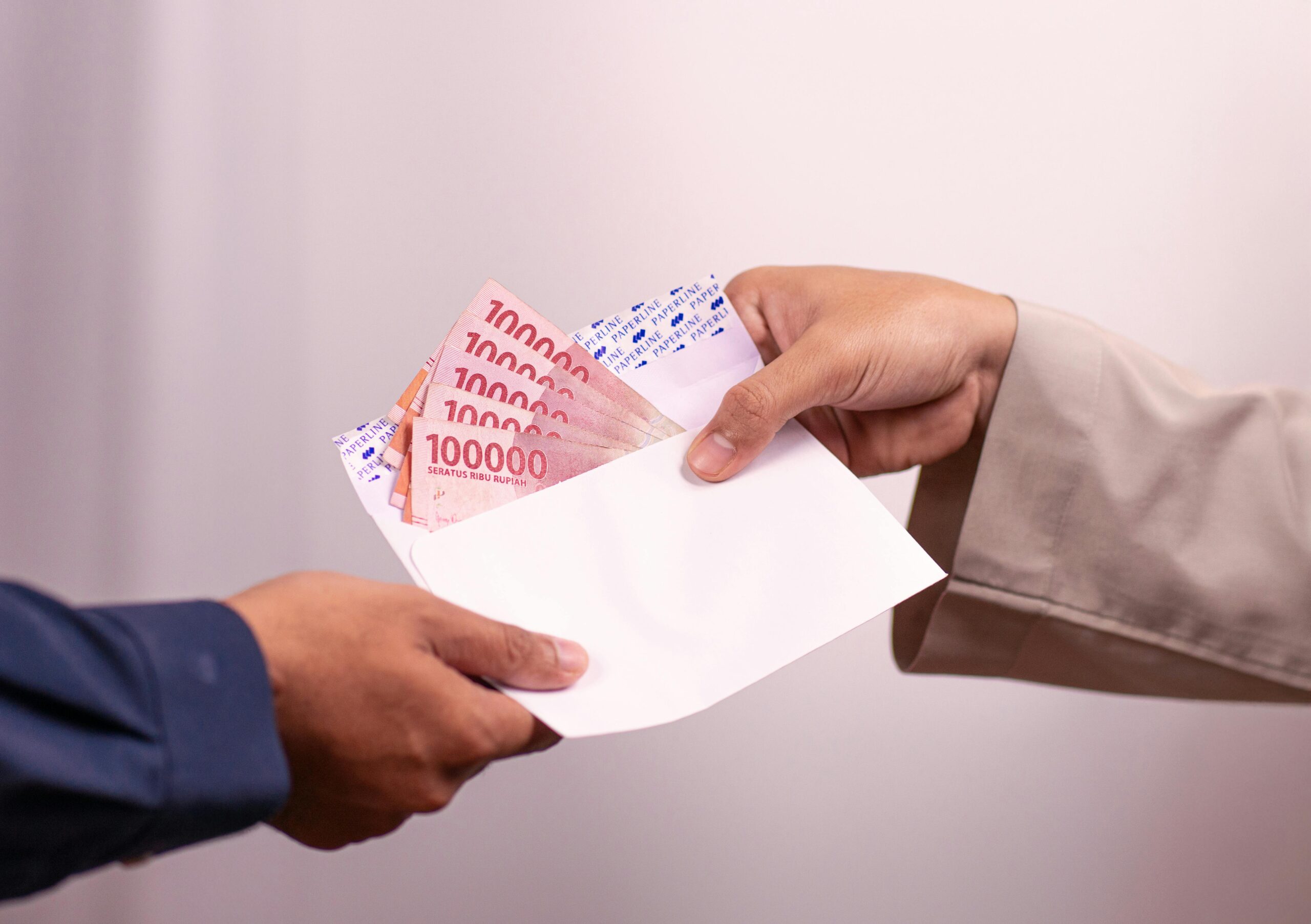 Hands giving and receiving Indonesian rupiah in an envelope, symbolizing financial transaction.
